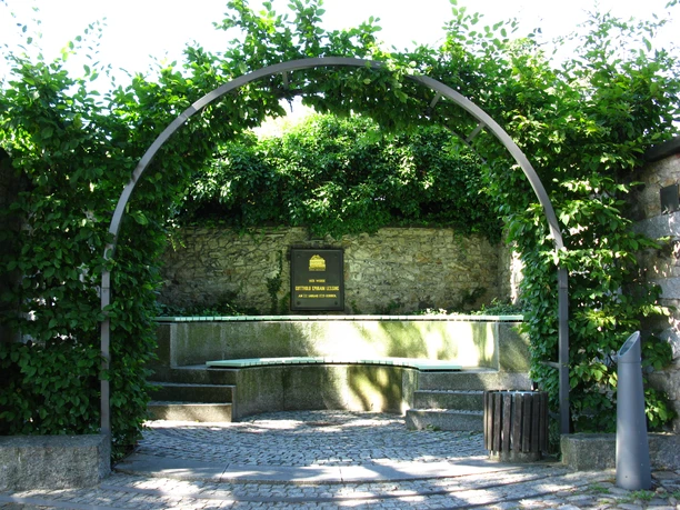 Lessing-Gedenkstaette Stadtverwaltung KM.jpg Grüne Gedenkstätte für Gotthold Ephraim Lessing mit Steinbank und Bogen aus Pflanzen.