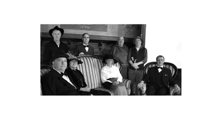 Das Bild zeigt eine Gruppe von acht Personen in historischer Kleidung, die Teil einer inszenierten Stadtführung zu sein scheinen. Die schwarz-weiße Fotografie hebt das klassische Ambiente und die unterschiedlichen Kostüme hervor.