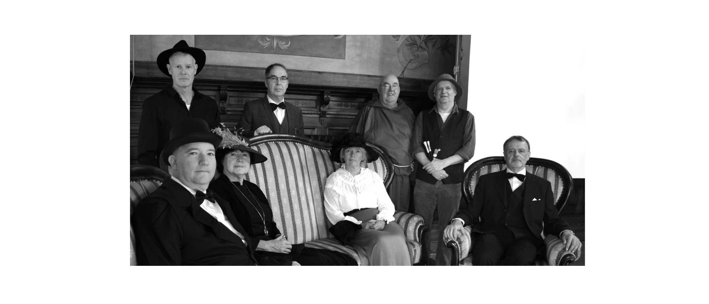 Das Bild zeigt eine Gruppe von acht Personen in historischer Kleidung, die Teil einer inszenierten Stadtführung zu sein scheinen. Die schwarz-weiße Fotografie hebt das klassische Ambiente und die unterschiedlichen Kostüme hervor.