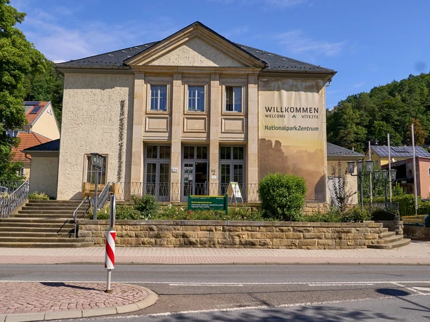 Nationalparkzentrum Klassisches Gebäude mit Säulen und "Willkommen im Nationalpark-Zentrum" Banner, vor blauem Himmel.