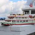 lego-weisse-flotte Modellschiff aus LEGO mit Aufschrift „Bad Zwischenahn“ vor echtem Fahrgastschiff am Seeufer
