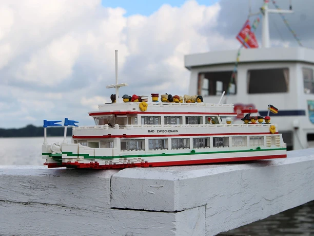 lego-weisse-flotte Modellschiff aus LEGO mit Aufschrift „Bad Zwischenahn“ vor echtem Fahrgastschiff am Seeufer