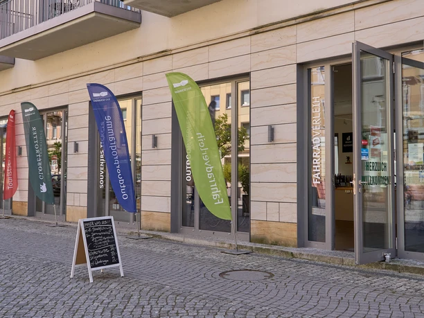 Colorful advertising flags in front of an entrance with a sign on the sidewalk.
