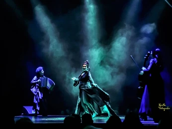 Cirque Bouffon - Célébration Dunkle Bühne mit dramatischer Beleuchtung und vier Musiker*innen in schwarzen Kostümen.Dark stage with dramatic lighting and four musicians in black costumes.