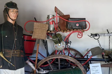 Man als etalagepop in uniform naast een historische brandweerfiets met uitrusting in een museum.