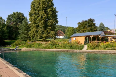 Freibad Goßdorf Freibad mit klarem Wasser umgeben von Bäumen und Terrasse vom Imbiss