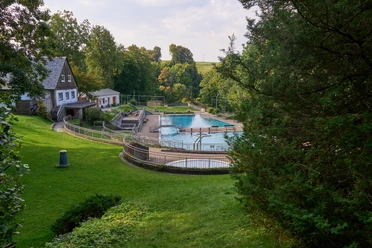 Freibad Stadt Hohnstein Freibad umgeben von grünen Bäumen und Wiese, neben einem Haus.