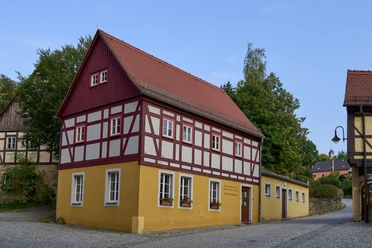 Touristinformation und Kaspermuseum Hohnstein Fachwerkhaus mit rotem Dach und gelben Wänden an einer Straßenecke.