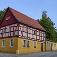 Touristinformation und Kaspermuseum Hohnstein Fachwerkhaus mit rotem Dach und gelben Wänden an einer Straßenecke.