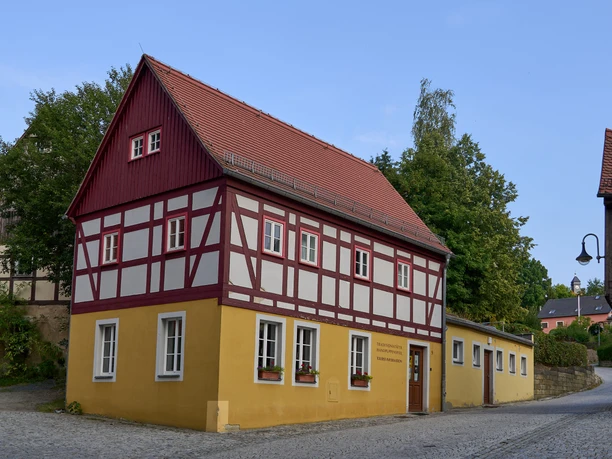 Touristinformation und Kaspermuseum Hohnstein Fachwerkhaus mit rotem Dach und gelben Wänden an einer Straßenecke.