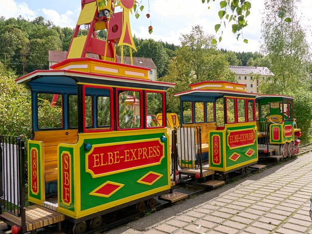 Kleurrijke kindertrein "Elbe-Express" staat op rails in een landelijke omgeving.