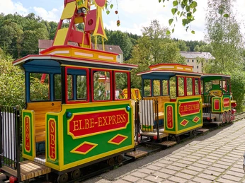 Elbefreizeitland Bunter Kinderzug "Elbe-Express" steht auf Schienen in einer ländlichen Umgebung.