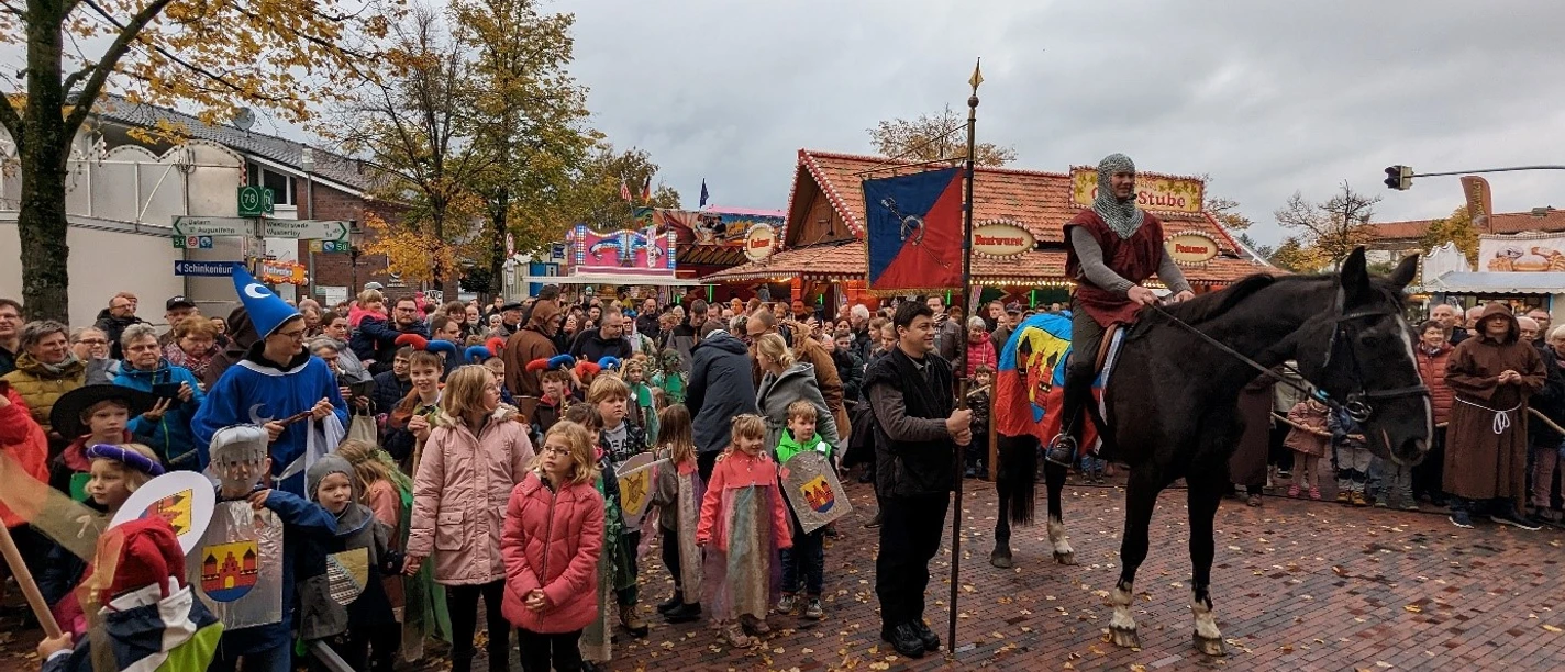 Ein Ritter reitet in historischer Kleidung, umgeben von feiernden Menschen.