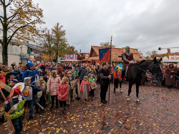 Aper_Markt_Ritter.jpg Ein Ritter reitet in historischer Kleidung, umgeben von feiernden Menschen.