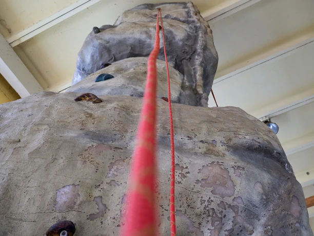 Indoor Hochseilgarten Kanuaktivtours Klimmuur van plastic met rode klimtouwgeleider binnenin.