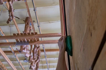Hand die groene handgreep vasthoudt tijdens het beklimmen van een houten muur op de achtergrond klimtoestellen aan het plafond.