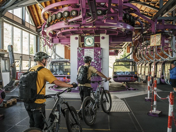 Transport des vélos en télécabine jusqu'au Bettmerhorn Bike Transport Aletsch Arena avec deux vététistes à l'entrée de la télécabine violette Bettmeralp-Bettmerhorn