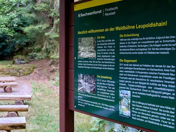 Informatiesteen op de voorgrond, houten banken en bomen op de achtergrond.