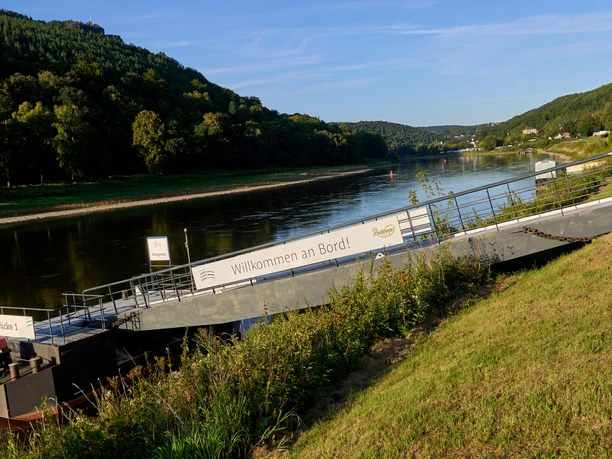 Elbe with landing stage and "Welcome aboard" sign, wooded hills in the background.