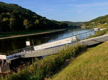 Dampfschiff Anlegestelle Königstein Elbe mit Anlegestelle und Schild "Willkommen an Bord", bewaldete Hügel im Hintergrund.