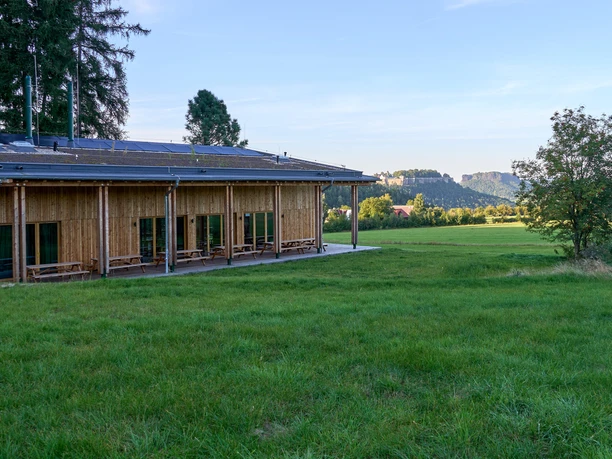 Walderlebniszentrum Dřevěná budova s velkými okny vedle zelené louky a stromů.