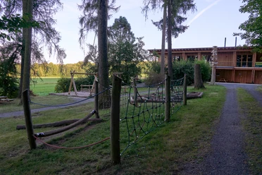Walderlebniszentrum-Leupoldishain-Koenigstein TVSSW-Yvonne-Brueckner-CCBY (4)web.jpg Holzhaus mit Spielplatz in einem bewaldeten Park.
