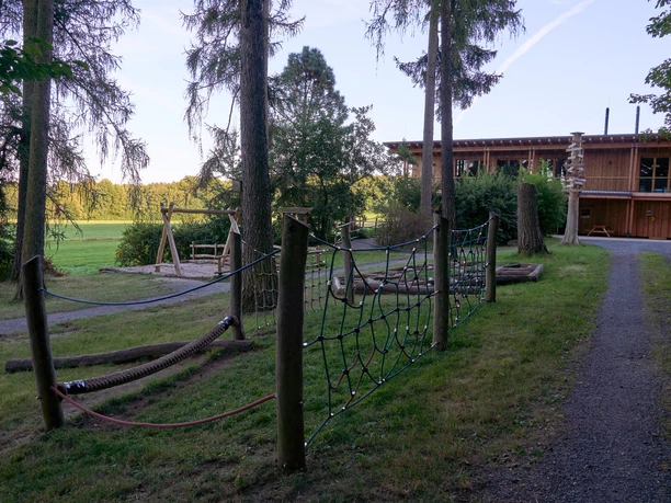 Walderlebniszentrum-Leupoldishain-Koenigstein TVSSW-Yvonne-Brueckner-CCBY (4)web.jpg Holzhaus mit Spielplatz in einem bewaldeten Park.