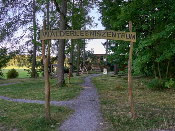Walderlebniszentrum Dřevěná cedule "Forest Experience Centre" nad cestou vedoucí do parku.