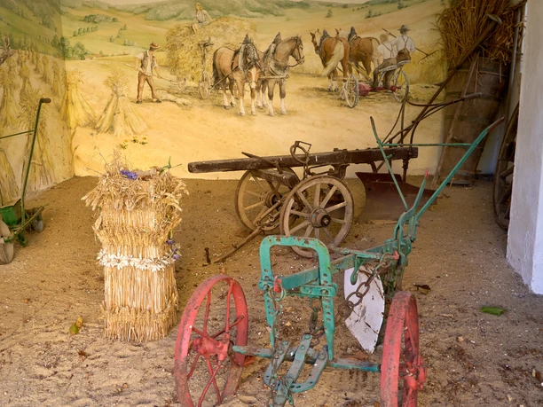 Oude landbouwmachines en karren in een schuur met muurschilderingen.