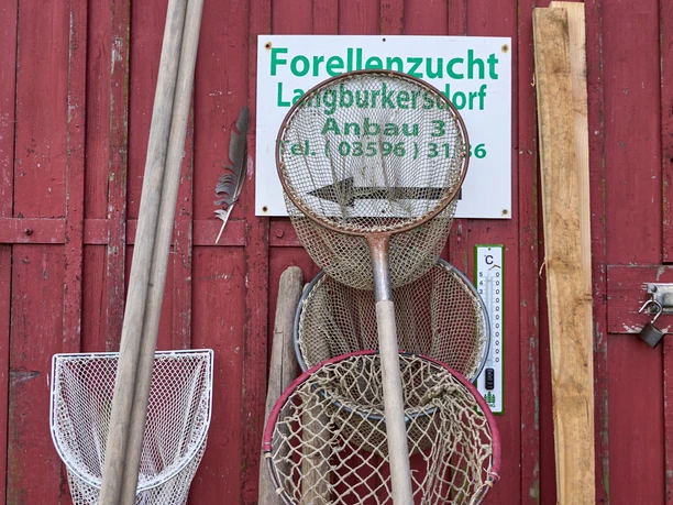 Fishing nets on red wooden wall with sign "Forellanzucht Langburkersdorf Anbau 3".