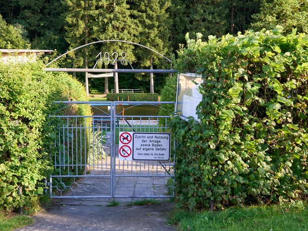 Waldbad Eingang Verschlossenes Tor mit Schild "Kein Zutritt für Unbefugte" umgeben von grünen Hecken.