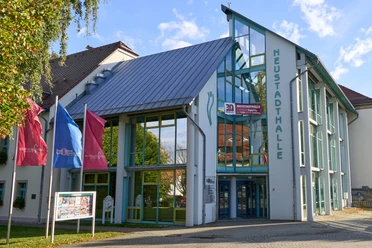 Modern glass façade of the Neustadthalle with blue roof and flags.