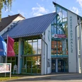 Tourismus Service Zentrum Neustadt (Sachsen) Moderne Glasfassade der Neustadthalle mit blauem Dach und Fahnen.