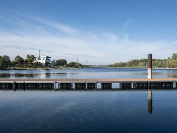 Lake Fühlingen Ein ruhiger See mit Steg, umgeben von Bäumen, unter einem klaren blauen Himmel.A calm lake with a jetty, surrounded by trees, under a clear blue sky.