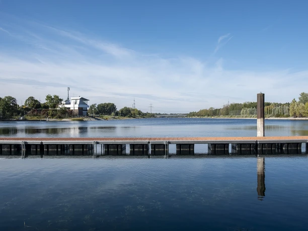 Lake Fühlingen A calm lake with a jetty, surrounded by trees, under a clear blue sky.