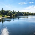 Fühlinger See Ein klarer See mit reflektierendem Sonnenlicht und umliegendem Grün unter blauem Himmel in Köln.A clear lake with reflecting sunlight and surrounding greenery under a blue sky in Cologne.