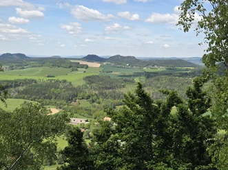 View of green landscape with trees and fields, blue sky.