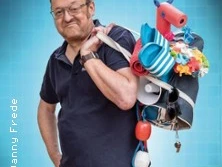 Ein Mann mittleren Alters lächelt, trägt eine Tasche voller bunter Poolspielzeuge.