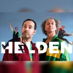 Zwei Männer in farbenfroher Kleidung posieren vor blauem Hintergrund mit "HELDEN"-Schriftzug.