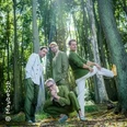 Vier Personen posieren spielerisch zwischen hohen Bäumen in einem lichtdurchfluteten Wald