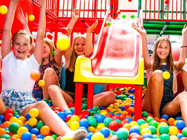 Kinder spielen fröhlich im bunten Bällebad unter einer roten Rutsche im Happylino Indoor-Spielbereich.