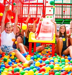 Action Cube im Happylino Kinder spielen fröhlich im bunten Bällebad unter einer roten Rutsche im Happylino Indoor-Spielbereich.