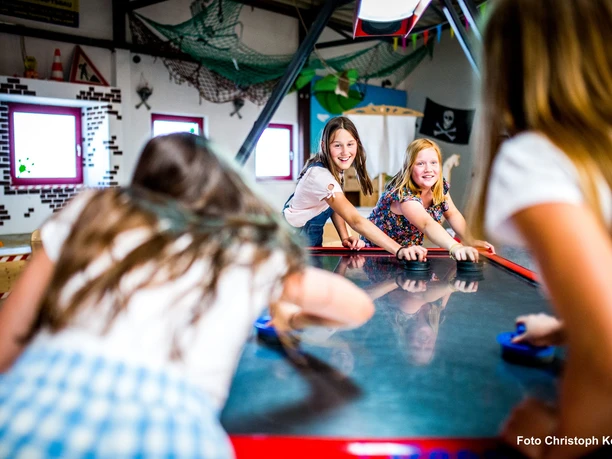 Kinder spielen fröhlich Airhockey in der bunten Happylino Indoor-Spielhalle mit Piratendekoration.