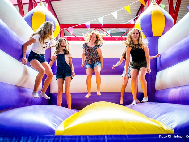 große Hüpfburg im Happylino Kinder springen lachend auf einer lila-gelben Hüpfburg in der Happylino Halle.
