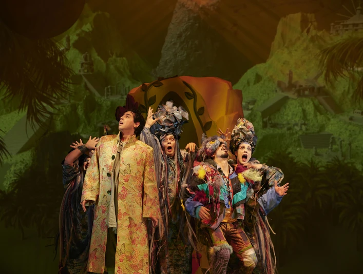 Vor einer bunten Bühnenkulisse stehen bunt kostümierte Operndarsteller.