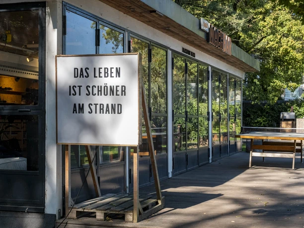Blackfoot Beach Wooden terrace with beach bar and table tennis table, surrounded by trees and sunshine.