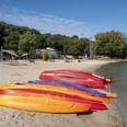 Blackfoot Beach Bunte Kajaks am Sandstrand eines Sees, umgeben von grünen Bäumen unter blauem Himmel.Colorful kayaks on the sandy beach of a lake, surrounded by green trees under a blue sky.