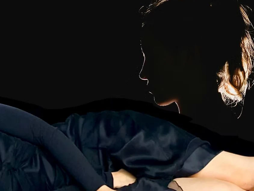 LUDER_Theater-K (c) Theater-K.jpg Schatten eines Gesichts und ein liegender Körper in schwarzem Kleid vor tiefschwarzem Hintergrund.