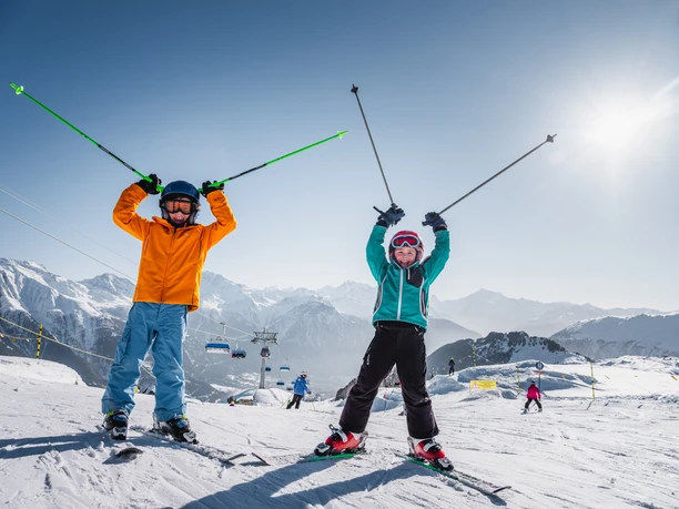 Skiing fun in a group under the winter sun Group ski pass Aletsch Arena with two children on the ski slope, laughing and with raised ski poles under a bright sun