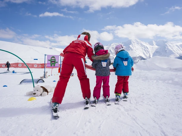 Cours de ski pour enfants au paradis de la neige de Bettmeralp Cours d'initiation au ski Bettmeralp avec monitrice de ski et deux enfants apprenant à skier au Kinderland
